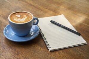 Xícara de café, caderno e caneta.