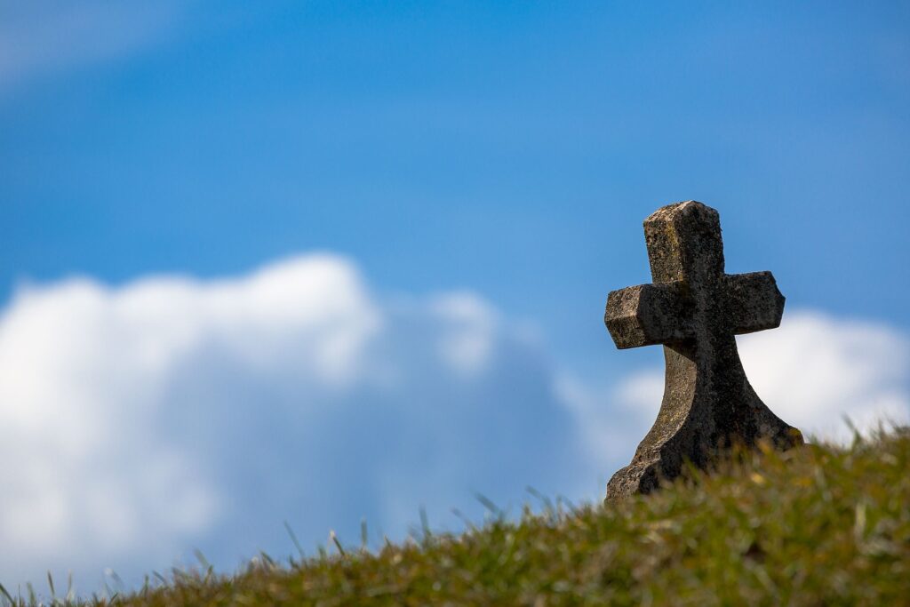 Imagem de um túmulo encimado com uma cruz, no campo.