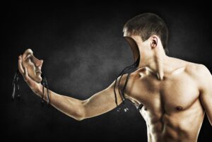 Imagem mostra um homem nu até a cintura, com o próprio rosto na mão, desconectado do crânio, com cabos eletrônicos à mostra em ambas as partes.